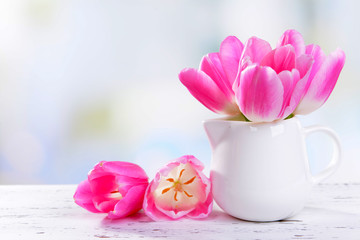 Beautiful tulips in bucket in vase on table on light background