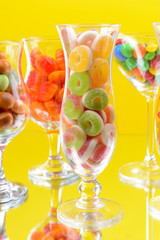 Different colorful fruit candy in glasses on yellow background