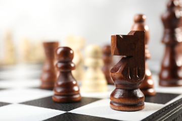 Dark brown wooden chess knight piece on checkered board with blurred background, strategic game play © Africa Studio