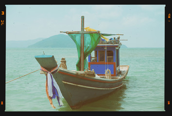 Small wooden fishing boat on tropical beach, retro film stylized