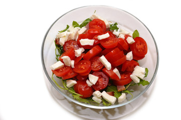 Mediterranean salad with feta cheese, tomato and rucola served in a bowl, isolated on white background