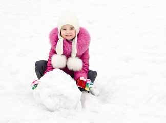 Cute smiling little girl makes snowman in winter day