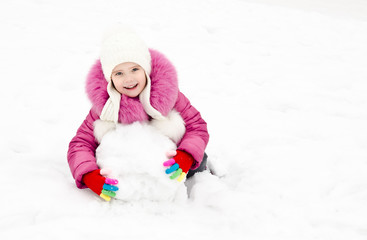 Fototapeta na wymiar Cute smiling little girl makes snowman in winter day