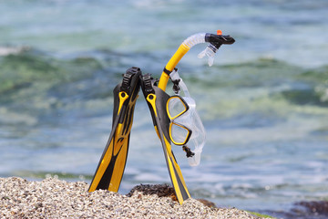 Flippers, mask and snorkel lying on sandy beach. Sea background