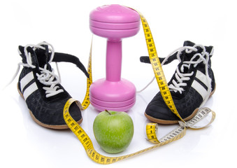 Pink dumbell, an apple and fitness shoes with a tape measure