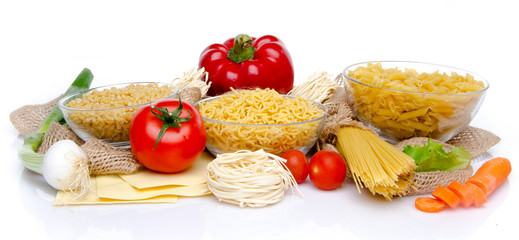 Different types of uncooked pasta and vegetables on a burlap