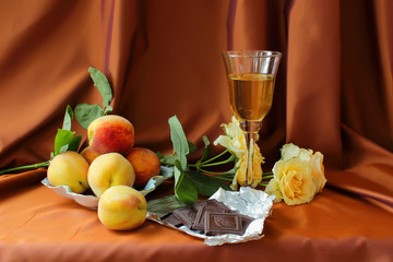 Glass of white wine, peaches, roses and chocolate bar.