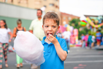 Cute kid eating cotton candy over fair background