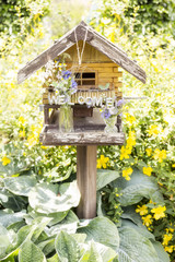 Vogelhaus mit Blumen und Schild Welcome