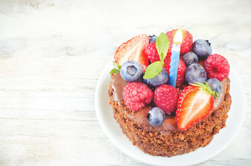 chocolate birthday cake with candle, raspberries, blueberries an
