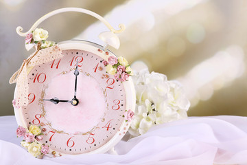 Beautiful vintage alarm clock with flowers on light background