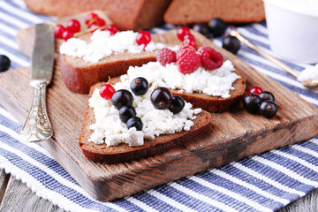 Bread with cottage cheese and berries on wooden board close-up