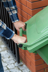 Male hands pushing a wheeled dumpster