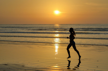 Fototapeta premium Silhouette of woman jogger running on sunset beach
