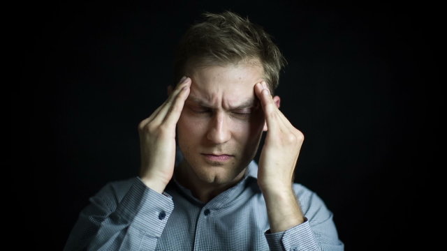 Portrait of stressed man with headache on black background