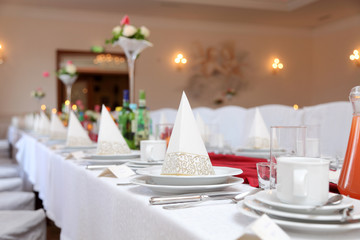 Stół weselny w restauracji z talerzami, filiżankami i sztućcami.