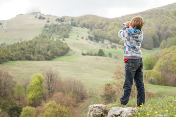 young child boy looking through binocular to the country side