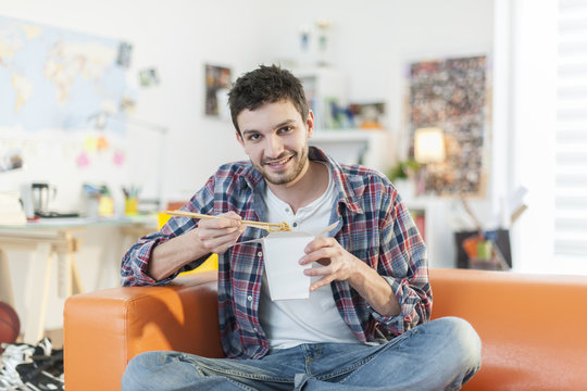 young man sitting on the couch eating Chinese noodles with chops