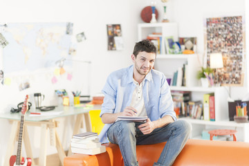 young student sits on a sofa is writing on a notebook