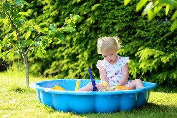 Happy little girl playing in sandbox in the garden on summer day
