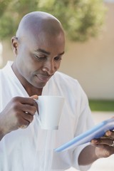 Handsome man in bathrobe using tablet at breakfast outside