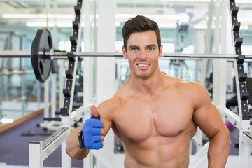 Fototapeta na wymiar Smiling shirtless muscular man giving thumbs up in gym
