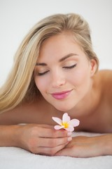 Obraz na płótnie Canvas Beautiful blonde lying on massage table smelling flower