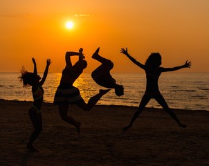 Silhouettes a young people having fun on a beach against sunset