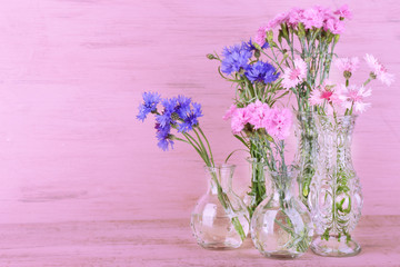 Beautiful summer flowers in vases on pink wooden background