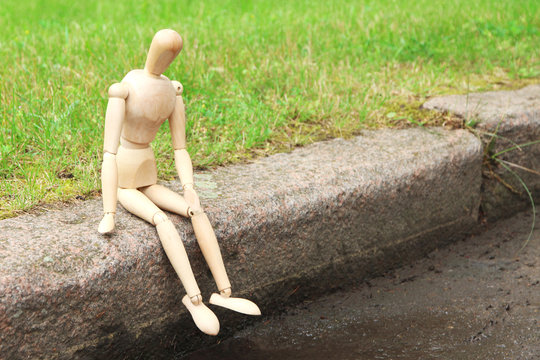 Wooden pose puppet sitting on stone, outdoors