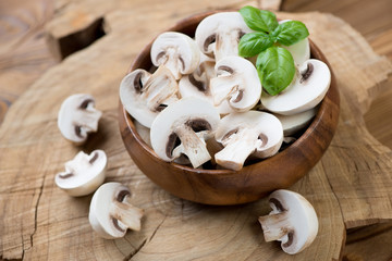Wooden bowl with raw sliced champignons and green basil