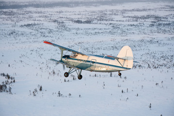 Old plane flying over the snow-covered plain