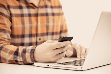 Close-up of man using mobile with laptop