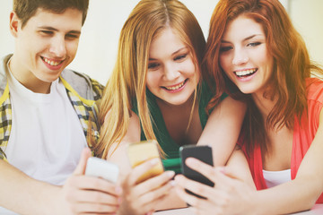 three smiling students with smartphone at school