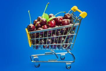 Shopping cart with fresh cherries on a blue background