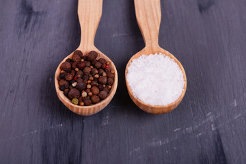 Salt and pepper in spoon on wooden table close-up