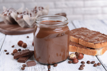 Sweet chocolate cream in jar on table on light background