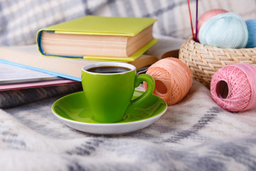 Cup of coffee and yarn for knitting on plaid with books