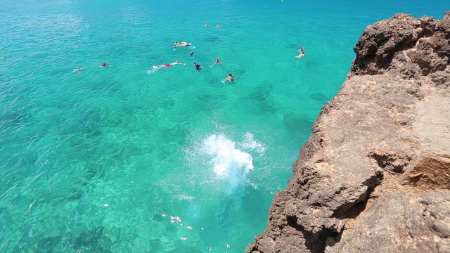 young woman doing a backflip from cliff into the ocean