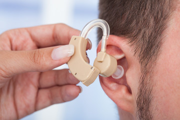 Doctor Inserting Hearing Aid In Man's Ear