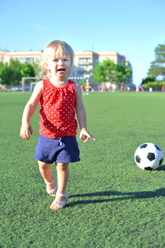 Young cheerful football fan girl on fresh green grass with ball