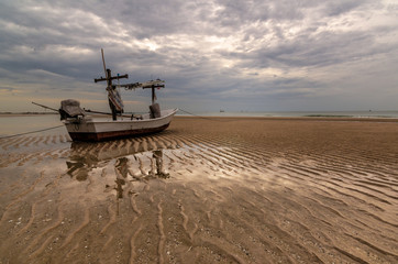 And old fishing boat beached on the sand during low tide with gloomy clouds overhead