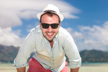 man with sunglasses and hat smiling on the beach