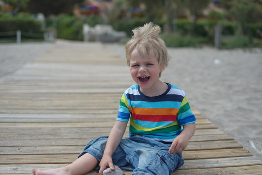 Flashy boy sits on a wooden walkway on the beach