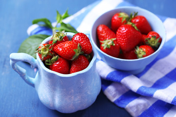 Ripe sweet strawberries in mugs  on color wooden background