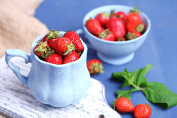 Ripe sweet strawberries in mug  on color wooden background