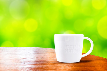 wood round table with white mug with green bokeh background