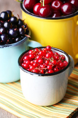 Summer berries in color mugs on color wooden background