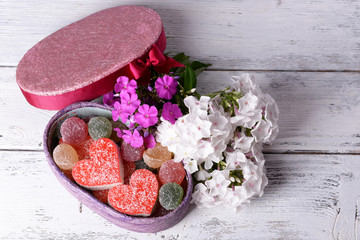 Present box with sweets and flowers on wooden background