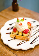 waffle with ice cream topping with strawberry and banana on wood